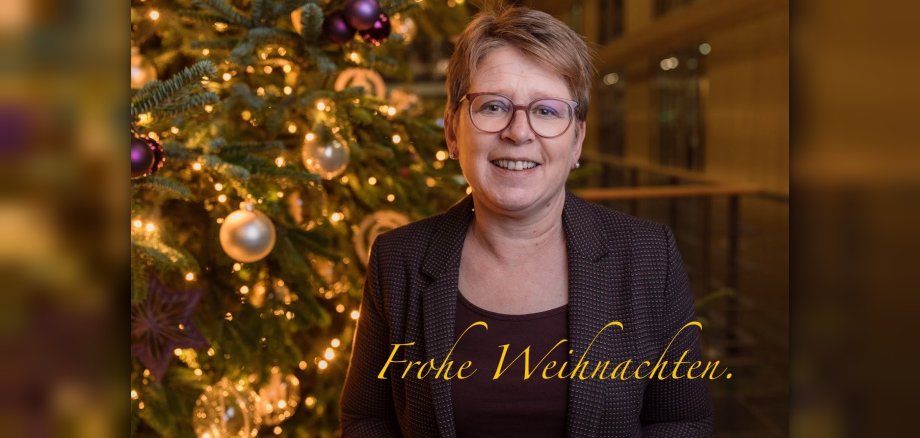 Tanja Machalet vor einem geschmückten Weihnachtsbaum, Kerzenlicht, am unteren Rand steht "Frohe Weihnachten"